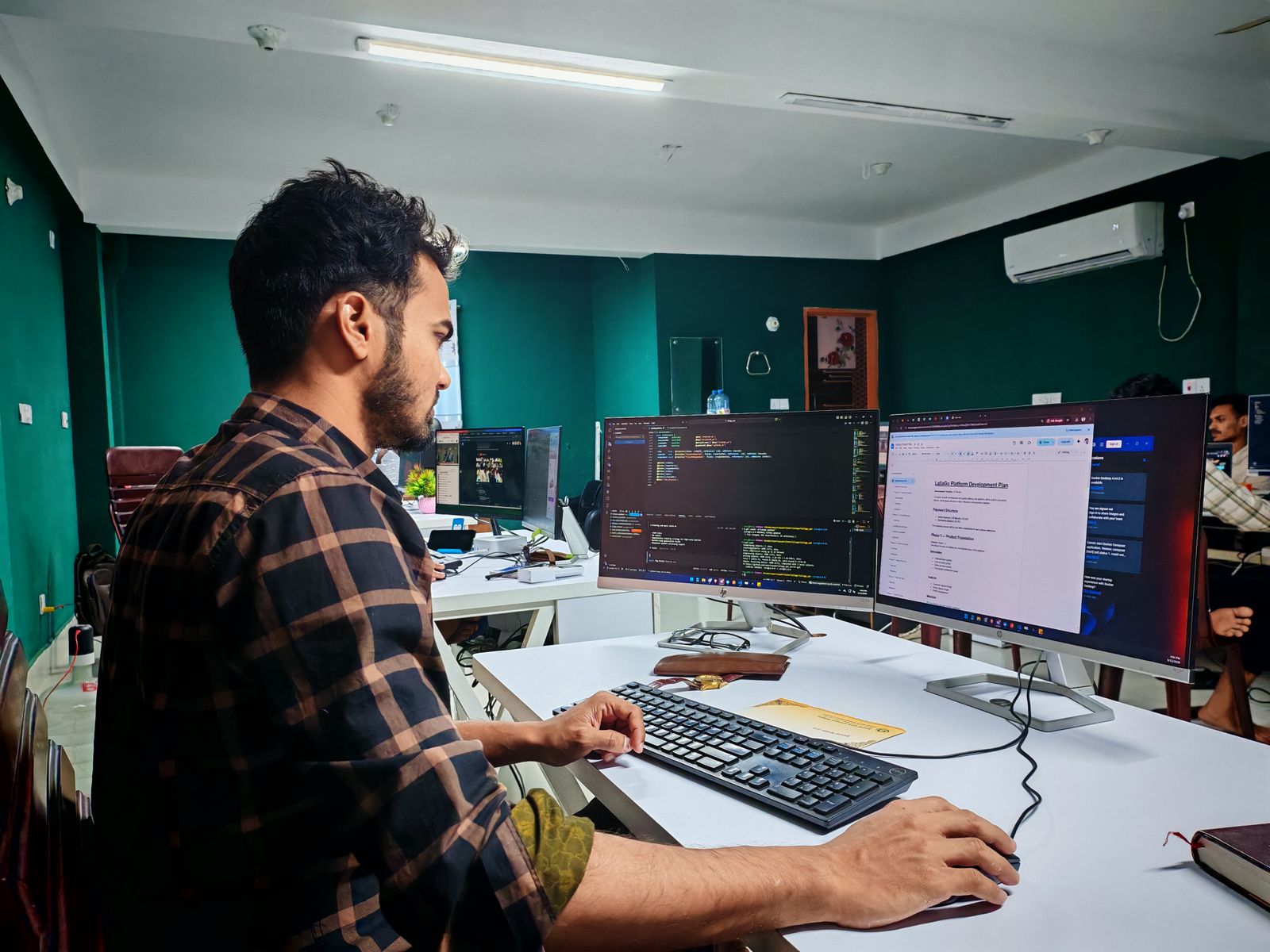 Softwareentwickler arbeitet an mehreren Bildschirmen in einem modernen Büro